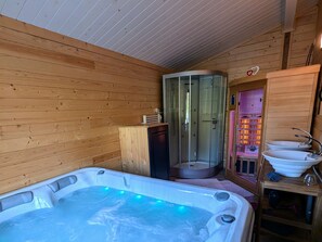 Una cabaña de madera con un jacuzzi, ducha cerrada con vidrio y un lavabo.