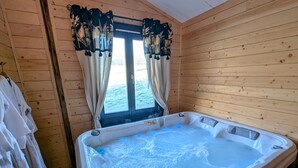 En stuga av trä med ett bubbelbad, gardiner och handdukar.