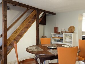 Ein Essbereich mit einem Holztisch, orangefarbenen Stühlen, einer weißen Regalanlage und einer Holztreppe.