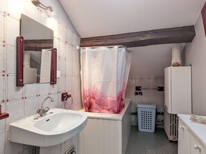 Ein Badezimmer mit weißem Waschbecken, einem Spiegel, einer Duschvorhang, einem Wäschekorb und einem Heizkörper.