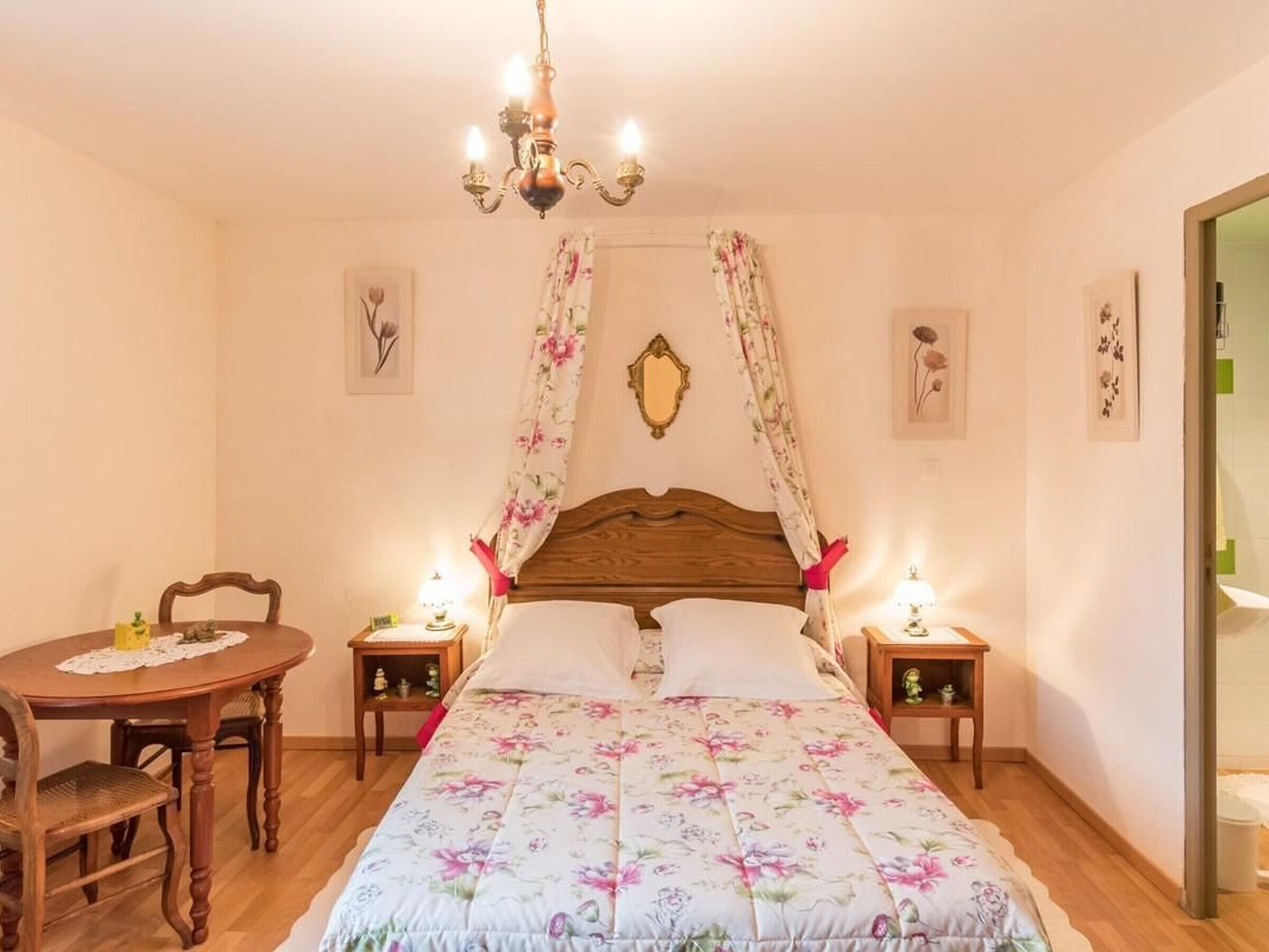 Une chambre à coucher avec un lit en bois, une literie à motifs floraux, un lustre, une table avec des chaises et des lampes de chevet.