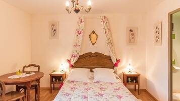Une chambre à coucher avec un lit en bois, une literie à motifs floraux, un lustre, une table avec des chaises et des lampes de chevet.