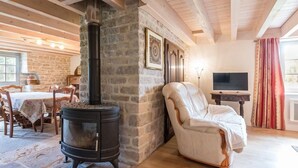 A cozy room with a stone fireplace, a comfortable armchair, a dining area with a table and chairs, and a television on a wooden table.