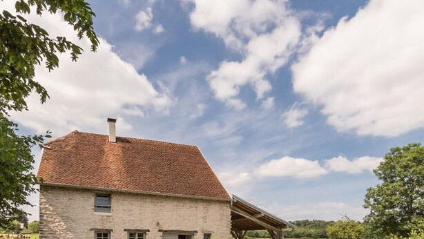 A stone house with a sloped roof, a covered porch, and a small garden area.