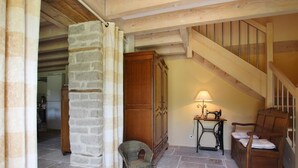 A rustic interior with a stone pillar, wooden staircase, and a cozy seating area with a lamp.