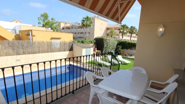 Ein Balkon mit Pool, weißen Plastikstühlen und einem Tisch.