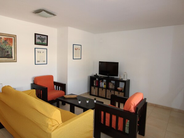 A living room with a yellow sofa, a red armchair, a black TV stand with books, and framed pictures on the wall.