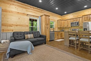 A cabin interior with a sofa, dining table, chairs, kitchen area, and wooden walls.