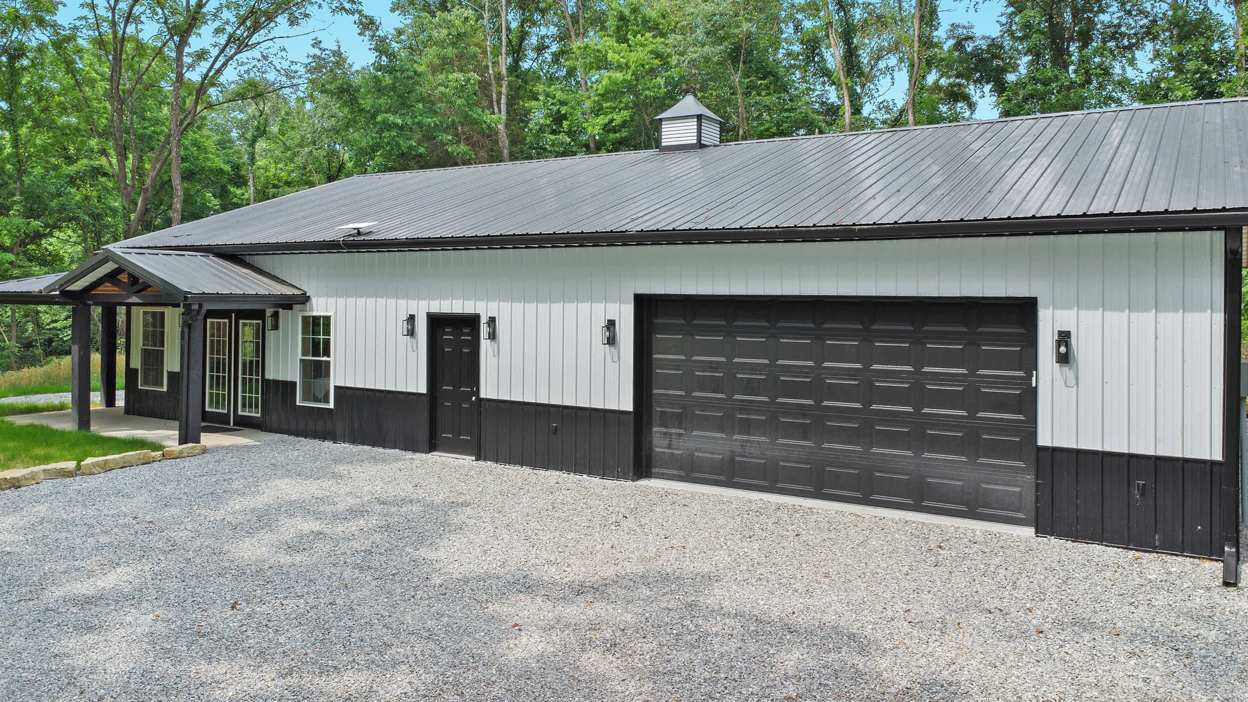 A building with a garage door, a covered porch, and a gravel driveway.