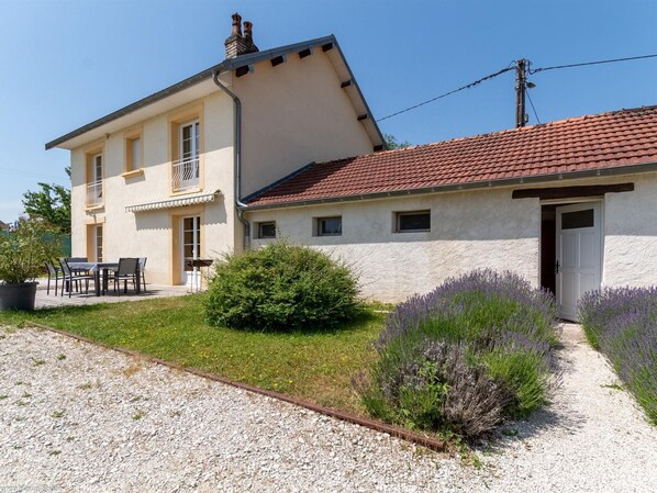 Ein zweigeschossiges Haus mit einem Schotterweg, einer Terrasse und Gartenmöbeln, sowie Lavendelsträuchern.