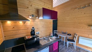 A compact kitchen with wooden walls, a built-in stove, a coffee maker, and a small refrigerator. - Cozy Chalet with Spa and Pets Allowed near Plombières-les-Bains (Fougerolles-Saint-Valbert)