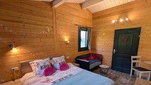 A cozy wooden cabin room with a bed, a small table, and a door. - Cozy Chalet with Spa and Pets Allowed near Plombières-les-Bains (Fougerolles-Saint-Valbert)