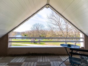 A room with a sloped ceiling and a large window overlooking a river and trees.