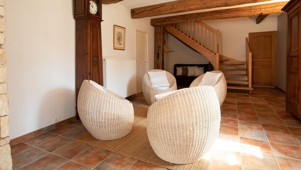 A rustic room with exposed wooden beams, a stone wall, a large clock, and wicker chairs. - Spacious house with garden and river view (Port-sur-Saône)
