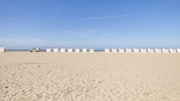 Ein sandiger Strand mit weißen Strandhütten und einem Fahrzeug in der Ferne.