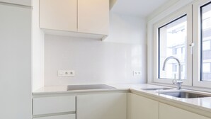 Eine moderne Küche mit weißen Schränken, einer Edelstahl-Spüle und einem Fenster mit Tageslicht.