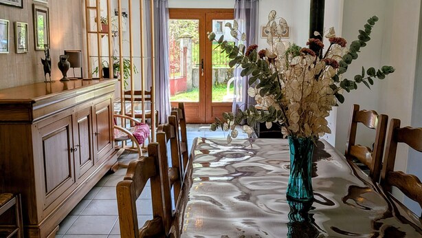 Un comedor con una mesa, sillas, un jarrón con flores, un aparador de madera y vistas al exterior a través de una puerta.