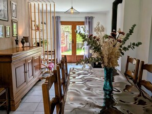 Un coin repas comprenant une table, des chaises, un vase de fleurs, un meuble en bois et une vue sur l’extérieur par une porte.