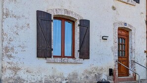 Un edificio con fachada desgastada, una puerta de madera y una ventana con contraventanas.