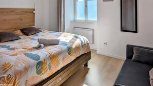 Un dormitorio con una cama de madera, una ventana con cortinas, un radiador, un espejo y un sofá.