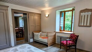 A room with a crib, a chair, a window with a view, and a door leading to another room. - Large house in the Vosges, nature escapes (Servance-Miellin-Miellin)