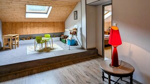 A cozy attic room with a sloped ceiling, wooden walls, a skylight, a dining area with chairs, a red lamp, and a child's play area with toys. - Large house in the Vosges, nature escapes (Servance-Miellin-Miellin)