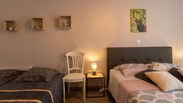 A bedroom with two beds, a chair, a bedside table with a lamp, and wall-mounted shelves with decorative items.