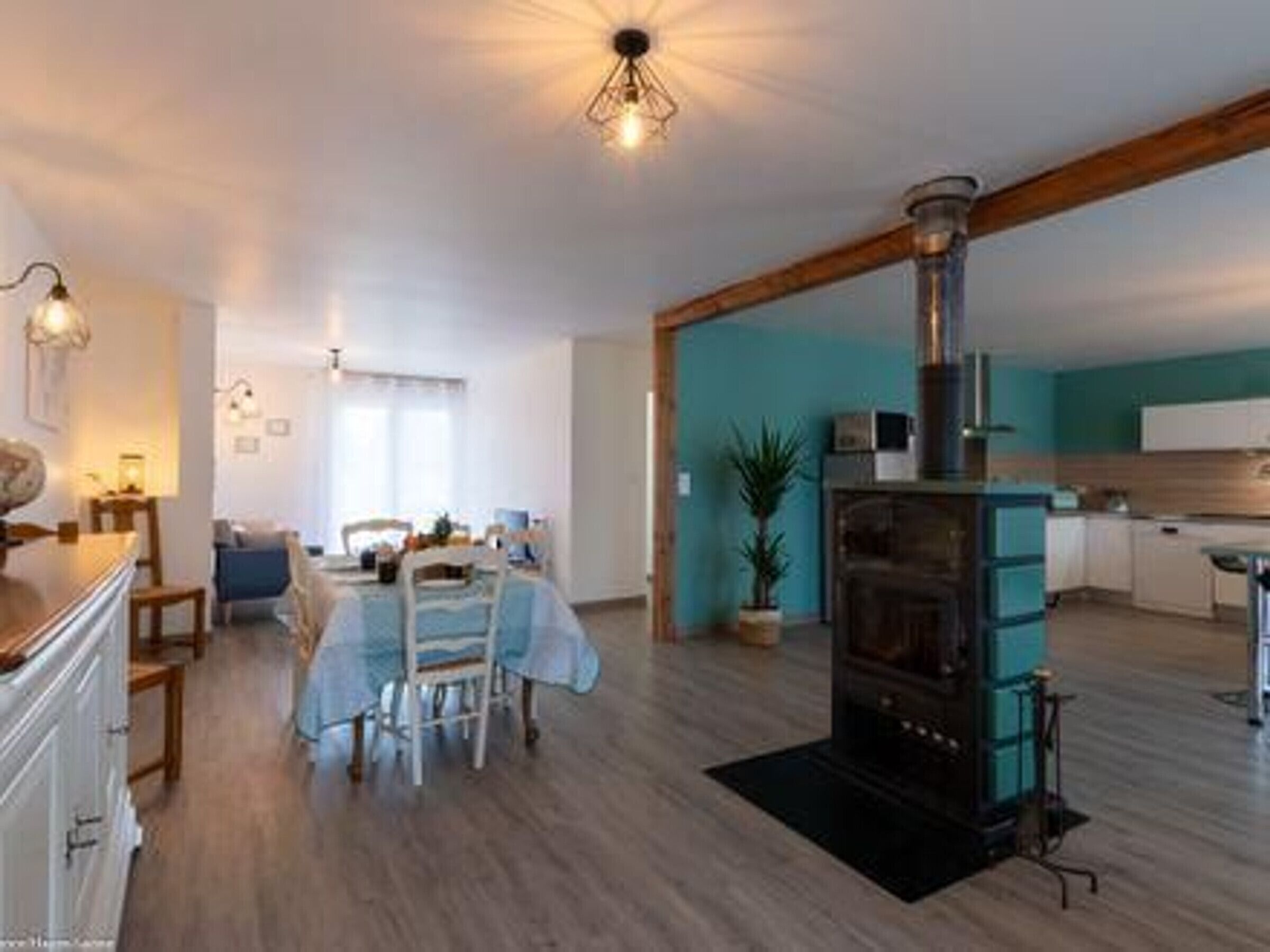 A modern kitchen with a central stove, wooden flooring, and a dining area with a table and chairs.