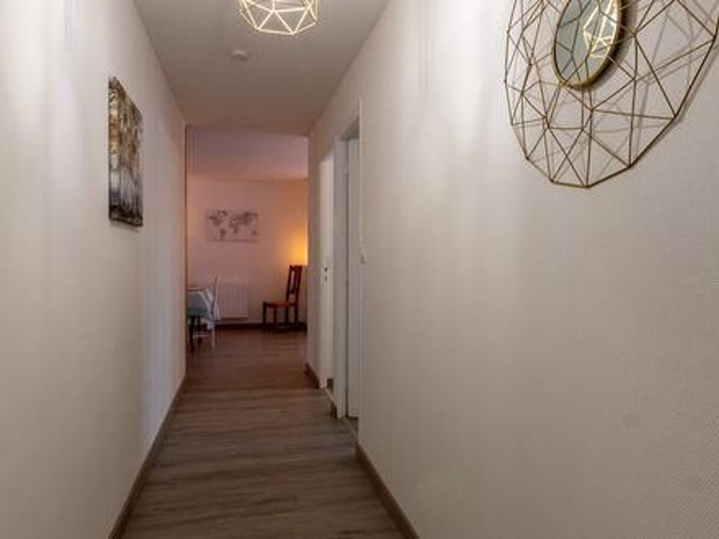 Un passadís estret amb terra de fusta, una decoració mural geomètrica i una porta al final.