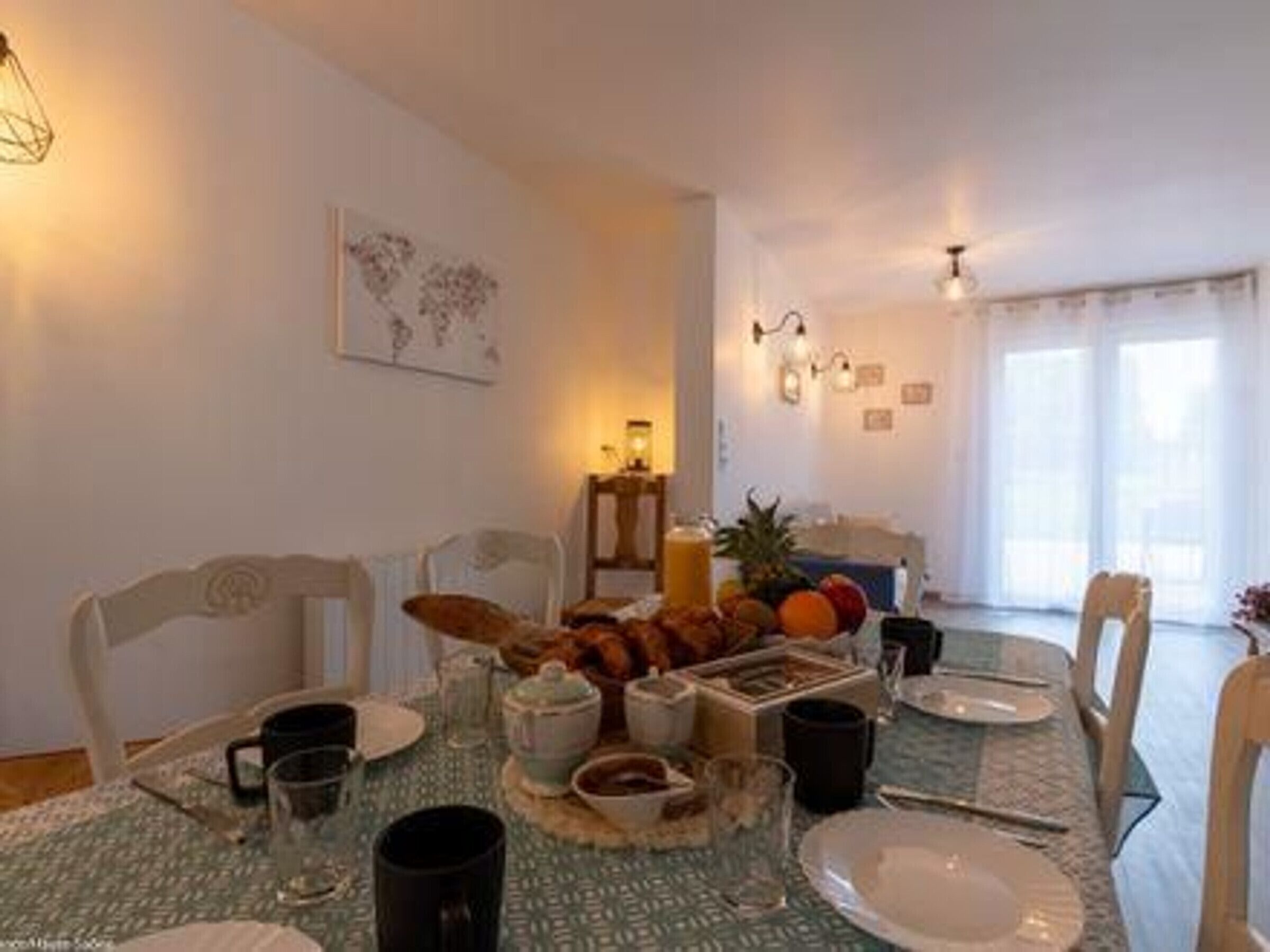 A dining area with a table set for breakfast, including fruits, pastries, and beverages.