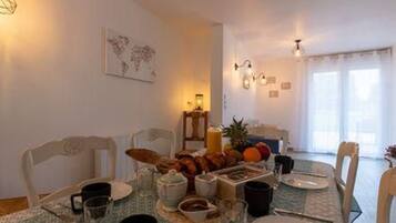 A dining area with a table set for breakfast, including fruits, pastries, and beverages.