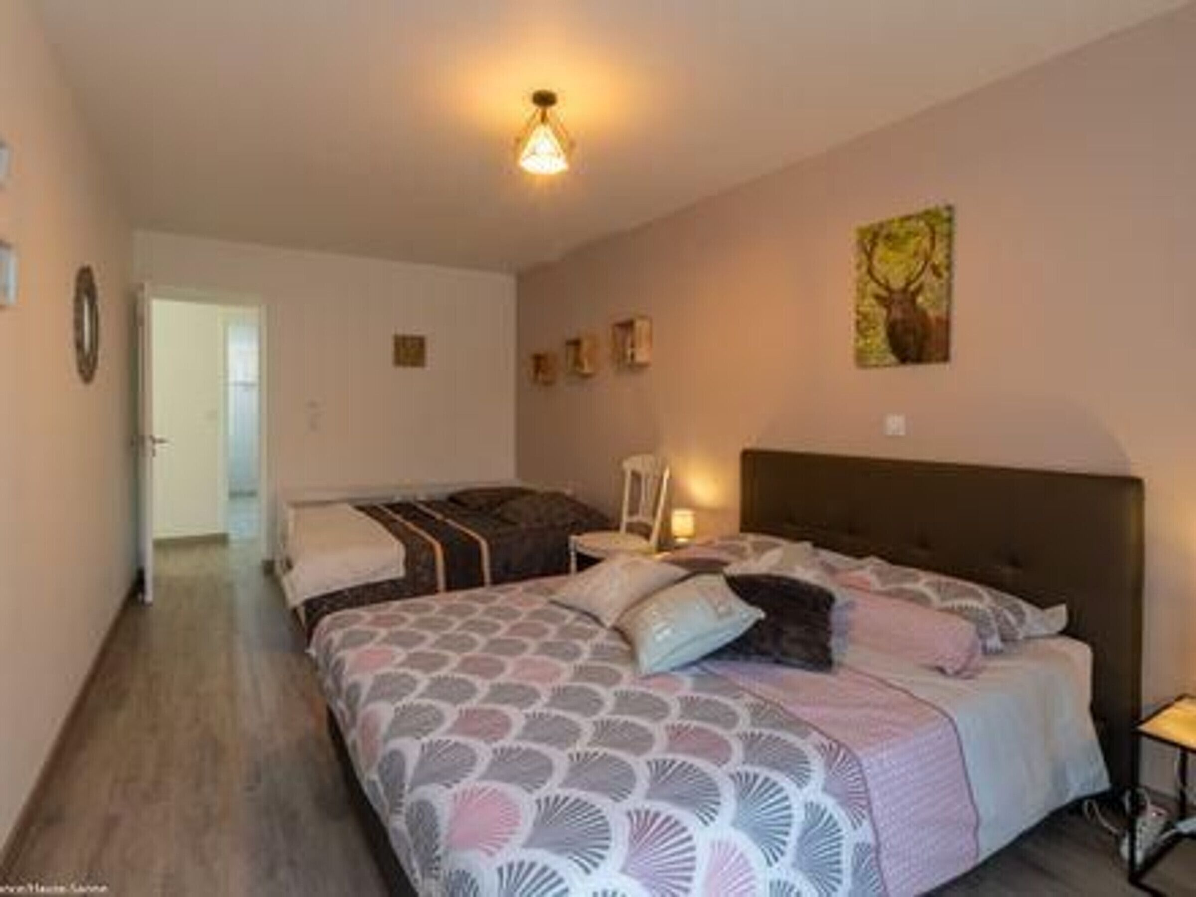 A bedroom with a bed, bedside tables, a nightstand, a wall-mounted lamp, and a painting.