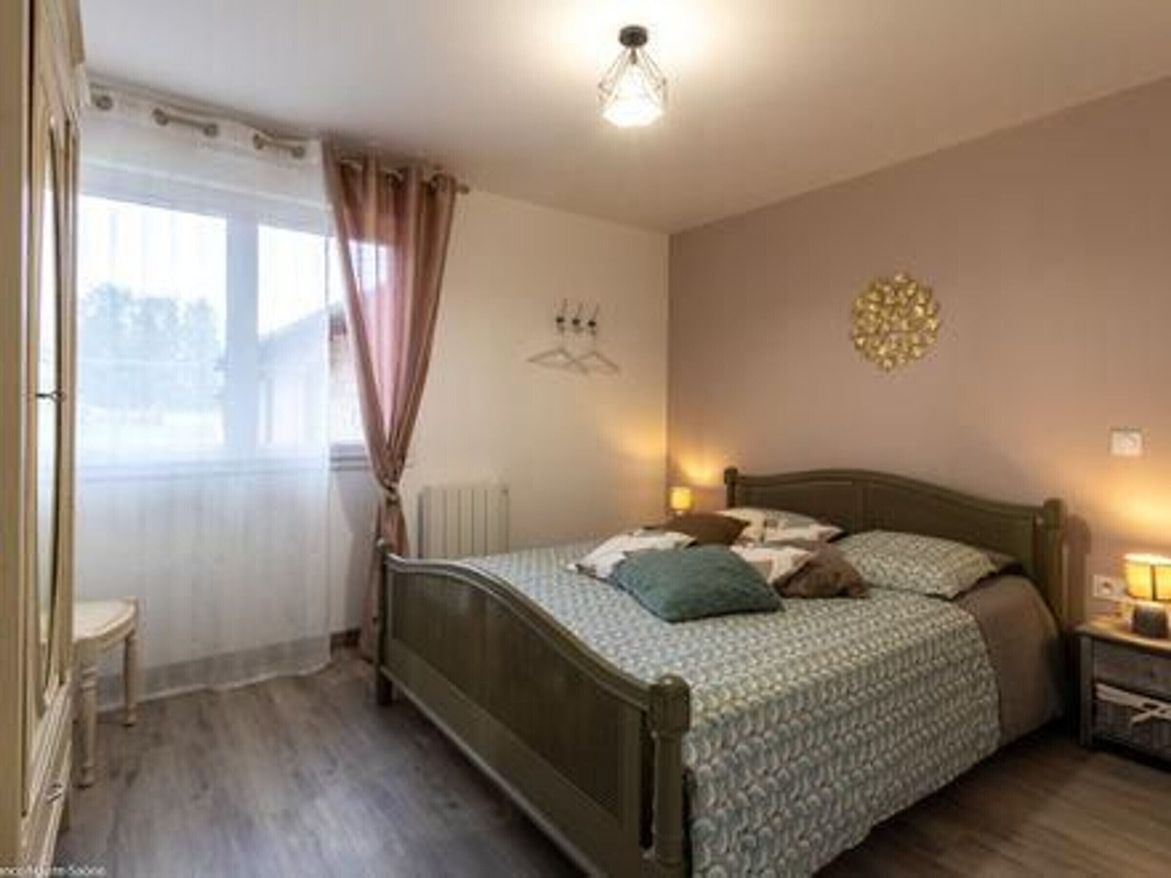 Un dormitorio con cama, mesita de noche y ventana con cortinas.