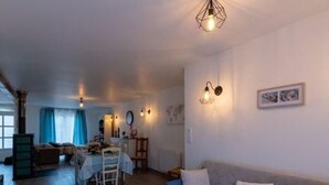 A cozy living room with a sofa, a dining table, and a kitchen area in the background. - Cozy modern cottage with garden, 2 bedrooms (Venisey)