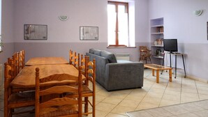 A room with a wooden dining table, grey sofa, and a television on a stand.