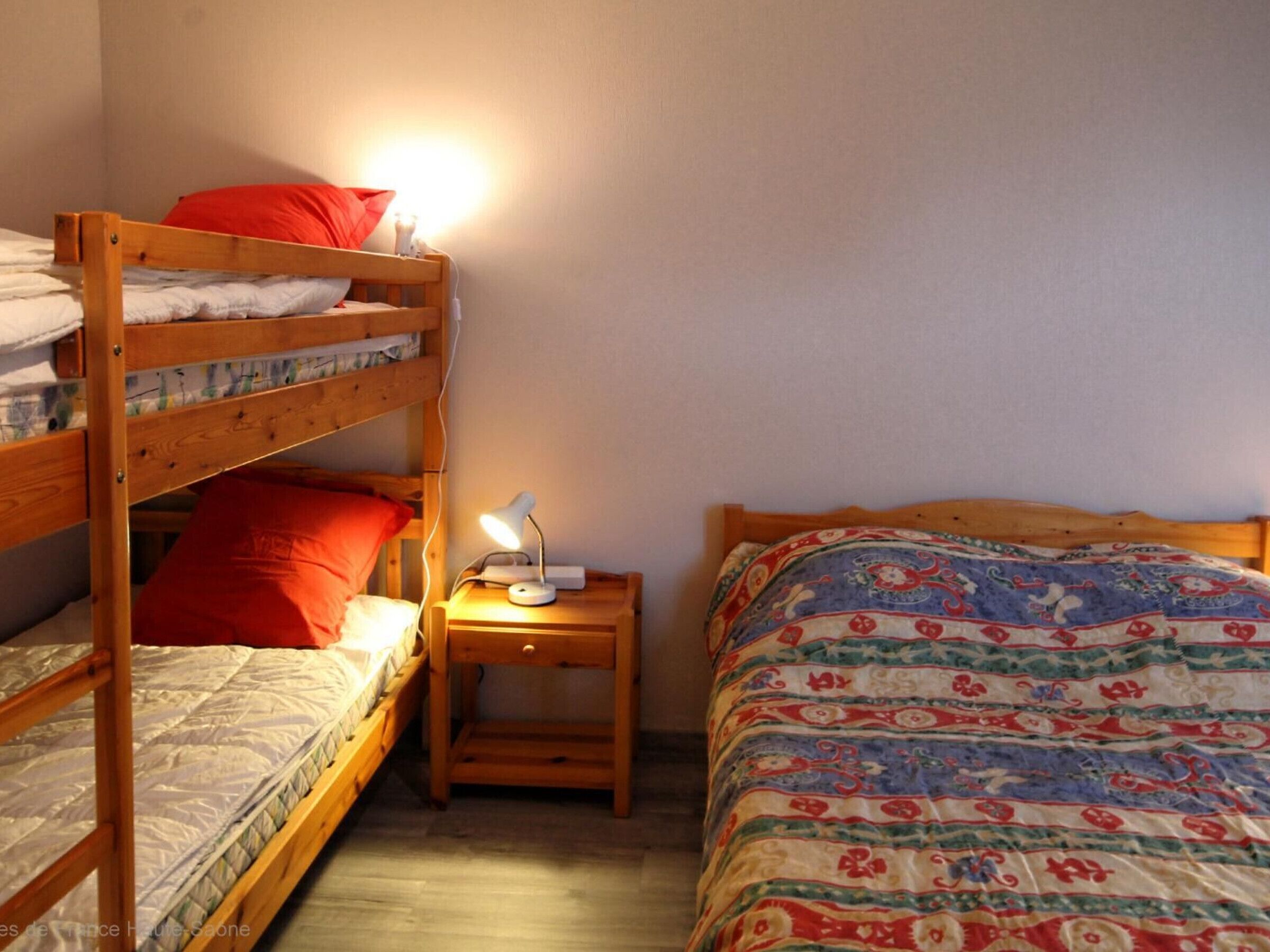 A bunk bed room with a bedside table, a lamp, and a patterned bedspread.