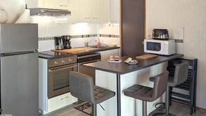 Une cuisine compacte avec des meubles blancs, un réfrigérateur en acier inoxydable, un four à micro-ondes, une machine à café et deux tabourets de bar.
