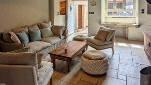 En hyggelig stue med sofa, lænestol og skammel, et træbord og et vindue med lukket persienne.