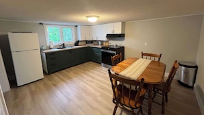 A compact kitchen with a dining table, chairs, a refrigerator, a microwave, and a stove. - Scout's House (Twillingate)