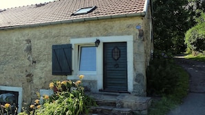 Una casa de piedra rústica con techo de tejas, un porche pequeño y una puerta con un ventanal decorativo encima.