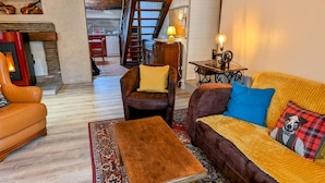 Una sala de estar acogedora con un sofá marrón, un sofá amarillo y una mesa de centro de madera. Se ve una escalera que conduce a otra habitación, y un cuadro en la pared.
