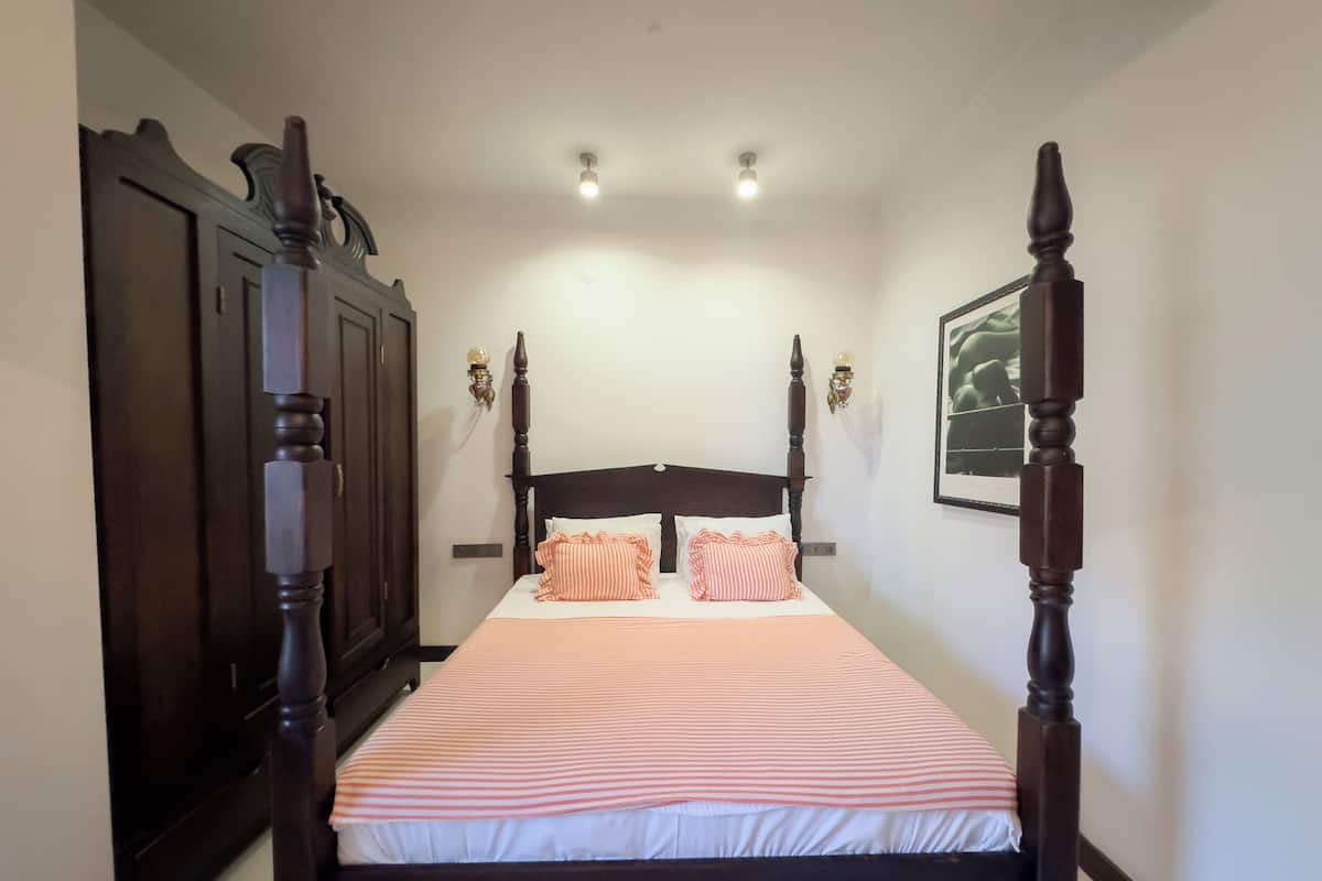 A bedroom with a four-poster bed, two wall sconces, and a framed picture on the wall.
