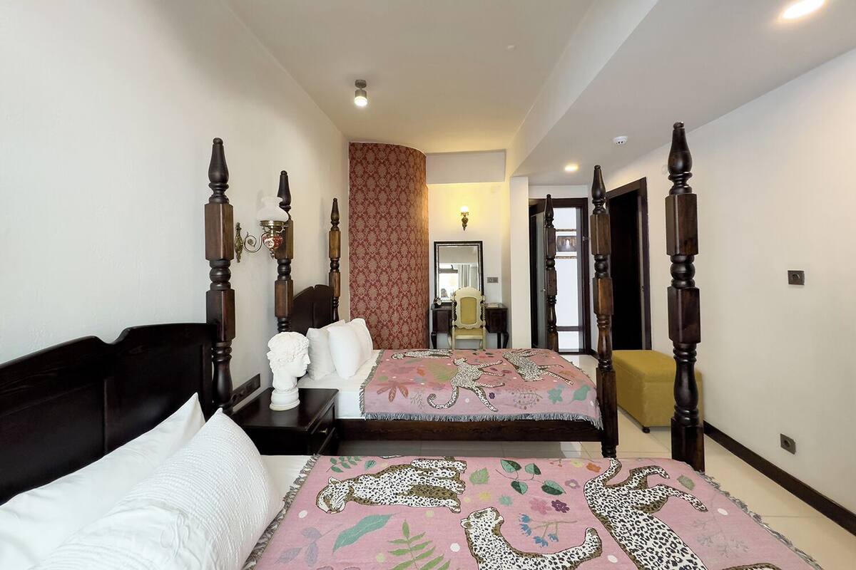 A bedroom with a four-poster bed, a nightstand, a mirror, and a decorative bust.