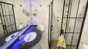 Une salle de bain moderne avec un lavabo en granit noir, deux miroirs ronds, une cabine de douche en verre et une serviette blanche suspendue à un porte-serviettes.