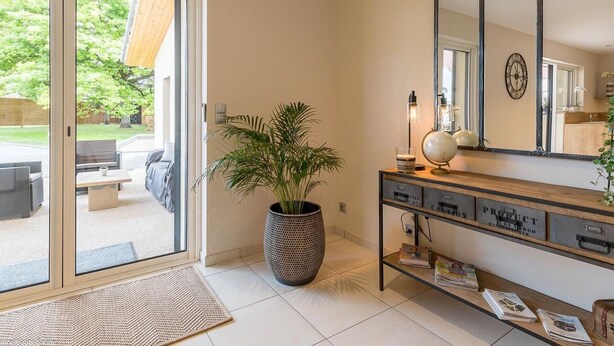 Et moderne interiør med en skydedør til en patio, et stort spejl og et konsolbord med blade og dekorative genstande.