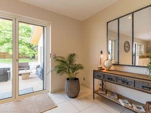 A modern interior with a sliding glass door leading to a patio, a large mirror, and a console table with magazines and decorative items. - Modern, bright lodging in Gy with spacious living area, garden, and children's games (Gy)