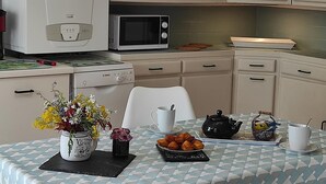 A kitchen with a microwave, stove, and cabinets. There is a table with a teapot, cups, and a basket of pastries.