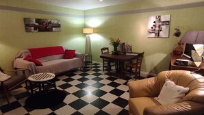 A living room with a checkered floor, a sofa, a leather armchair, a dining table with chairs, and a lamp.