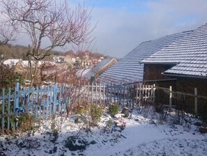 A snow-covered garden with a blue fence, a brick building, and a metal roof structure.