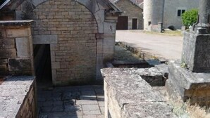A stone pathway leading to a brick archway, with a stone wall and a cylindrical structure in the background.